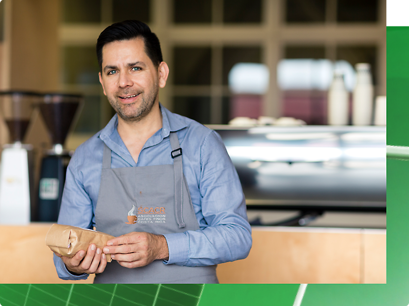 Uomo con un grembiule grigio che regge una busta di caffè.